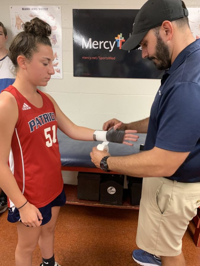 Trainer Mike Tzianos wraps the wrist of field hockey player Sophie Beckemeyer before a game. 
