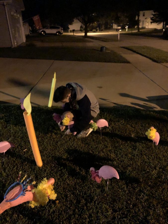 Working in the dark, senior Aaron Bennett sticks flamingos and birthday candles in a yard over the summer during the senior class flocking campaign.