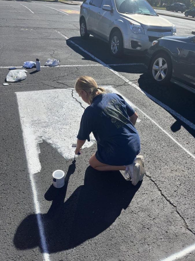 Senior+Caroline+Knolhoff+uses+white+paint+to+paint+a+basecoat+on+her+parking+spot+before+painting+her+design.+Knolhoff+was+one+of+only+4+seniors+who+chose+to+paint+their+parking+spot.