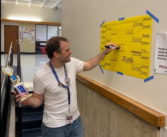 Art teacher Eric Ludlow writes his name on the bracket as the champion of Marshmallow Madness in 2023.