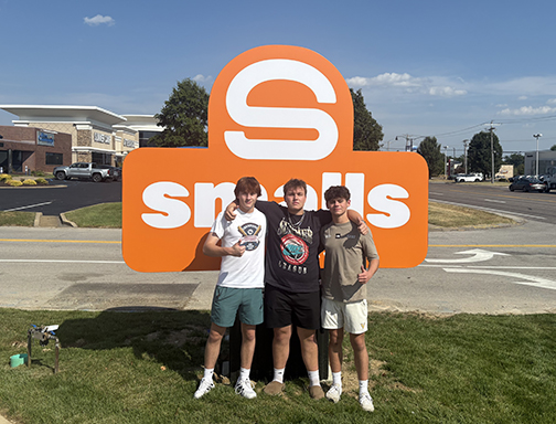 Writer Henry Mannion takes a picture in front of the Smalls Sliders sign with juniors Carter Holmdahl and Greyson Fears. 