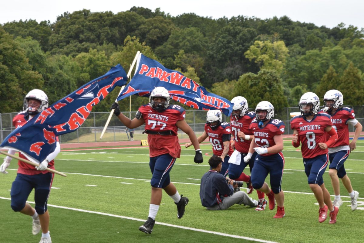 Senior Grant Williams waves the flag as the varsity Patriot football team rushes onto the field, excited for the first home football game of the year. 