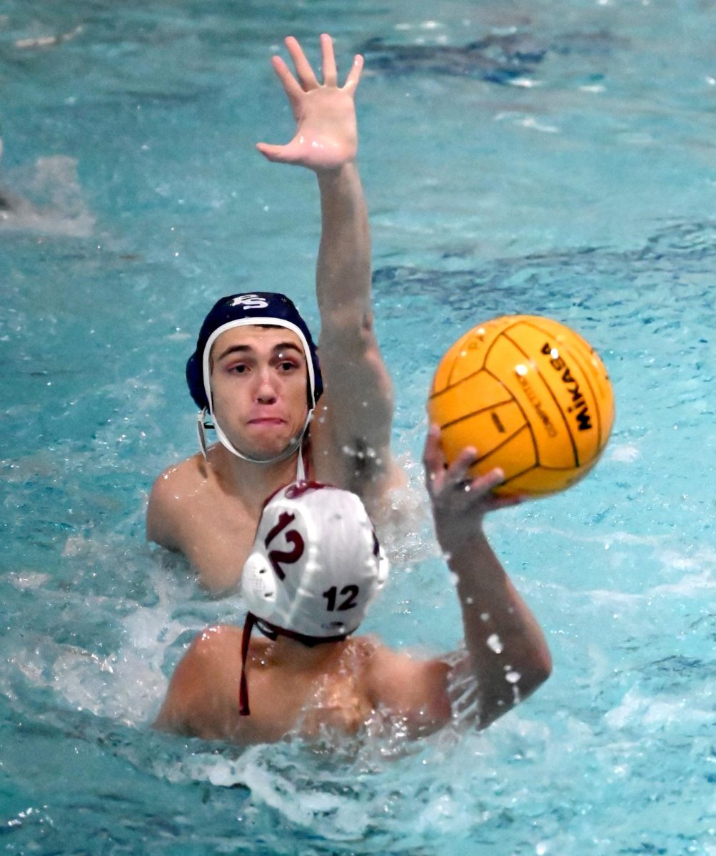 Putting his left hand up to block the ball, junior Charlie Shaffer plays defense in the water polo match against MICDS, March 30. The Patriots won, 20-5.