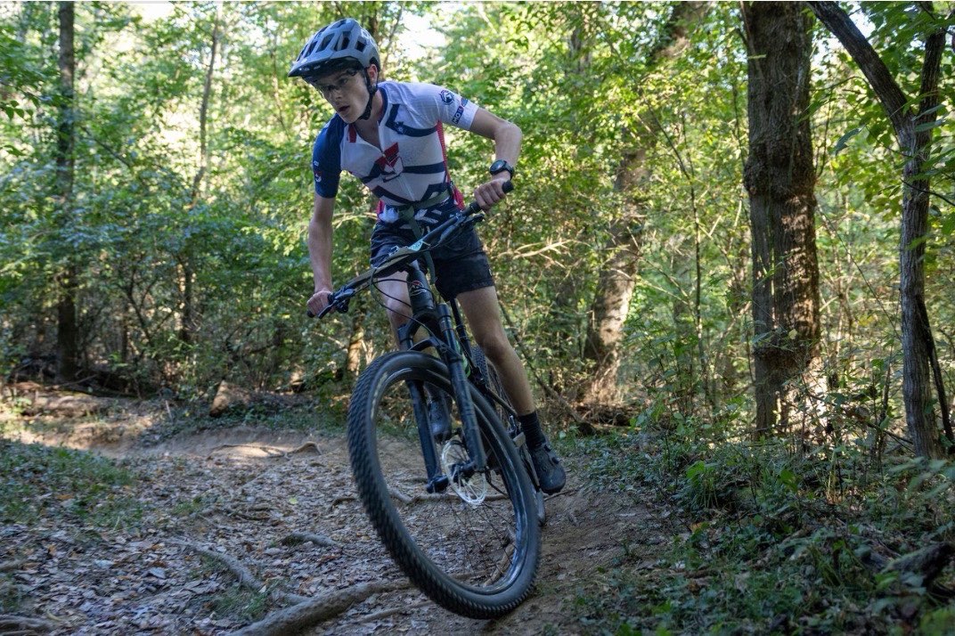 Racing for NICA (National Interscholastic Cycling Association), Noah McCallum makes a turn to stay on course, trying to finish in the valley park dirt crit race.